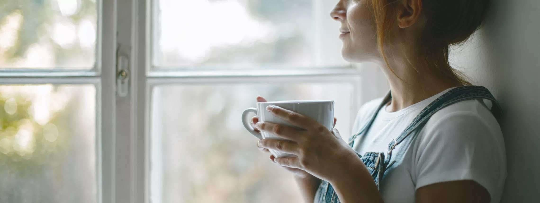 Psoriasis-Betroffene sitzt mit Tasse und schaut aus dem Fenster